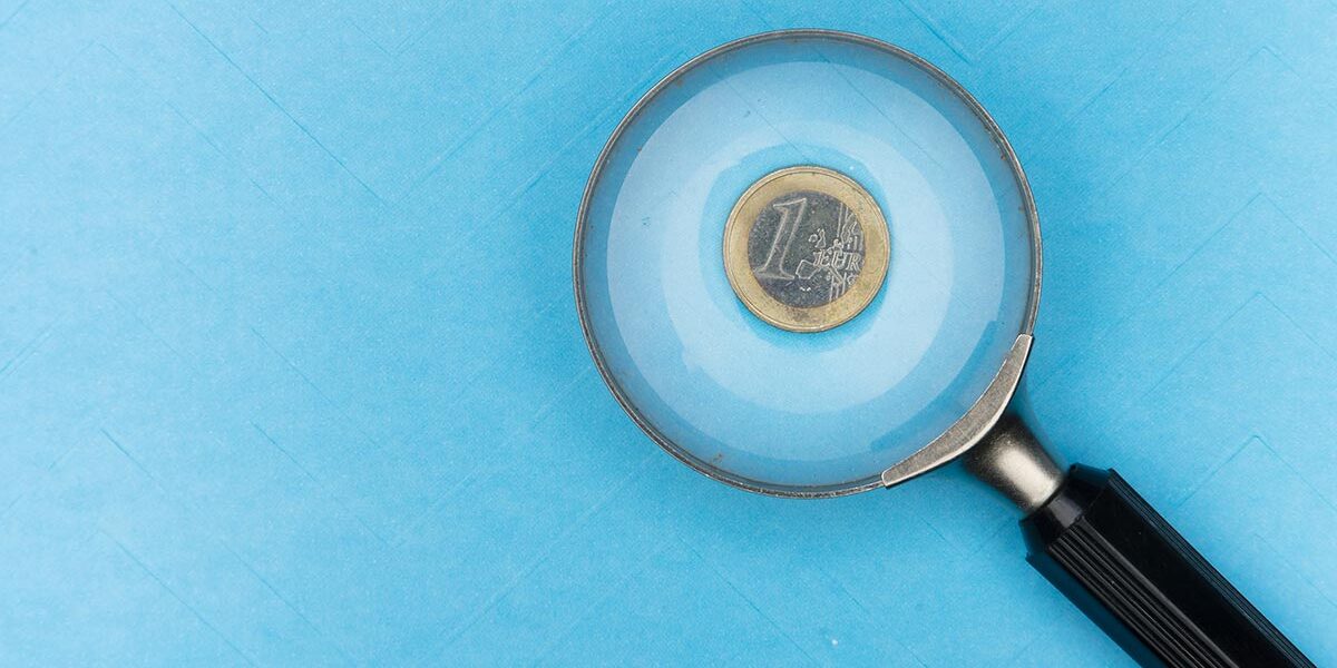 Immobilienfinanzierung Auf einer blauen Unterlage, unter einer Lupe liegt eine 1-Euro-Münze, was symbolisiert, dass man bei der Immobilienfinanzierung ganz genau aufs Geld schauen muss | Immobilienfinanzierung