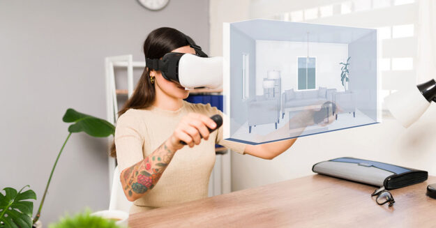 Eine Frau mit VR-Brille und jeweils einem Controller in ihren Händen besichtigt in ihrem Wohnzimmer eine Immobilie, die symbolisch vor ihr virtuell dargestellt ist | Virtuelle Immobilienbesichtigung