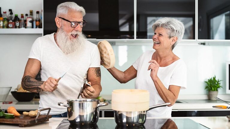 Wohnen im Alter Ein Seniorenpaar steht glücklich in der neuen, kleineren und altersgerechten Wohnung und albert herum | Wohnen im Alter