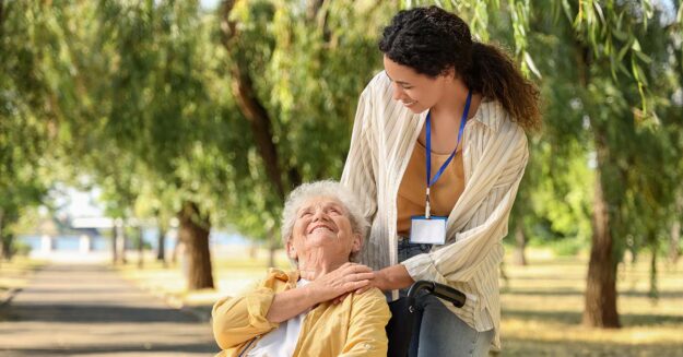 Eine Seniorin in ihrem Rollstuhl und ihre Pflegerin